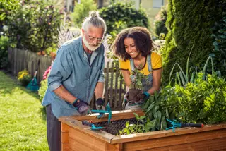 a woman standing next to the plants in her apartment with a packed travel bag